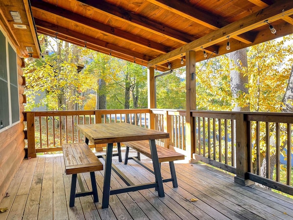 Une terrasse en bois, agrémentée d’une table de pique-nique et de bancs, entourée d’une rambarde, et offrant une vue sur une forêt aux couleurs automnales.