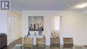 Relax in a stylish living room with a glass dining table and comfortable seating for four, surrounded by a beautiful abstract art piece.