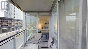 Enjoy the urban view from this balcony with a glass railing, two chairs, and a small table.