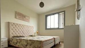 Un dormitorio con una cama grande, una mesita de noche, un aparador, una ventana con persianas y una lámpara en el techo.