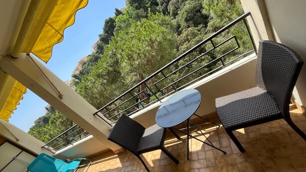 Un balcón con mobiliario de mimbre, una mesa redonda pequeña y vistas a una ladera boscosa.