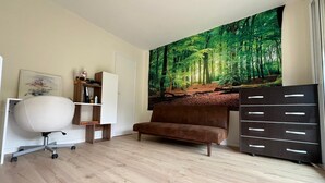 Una habitación moderna con un mural grande de temática forestal, un sofá marrón, un escritorio blanco con una silla y un aparador oscuro con cajones.
