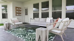 Une terrasse couverte avec des meubles en osier, un canapé blanc et un tapis à motifs.