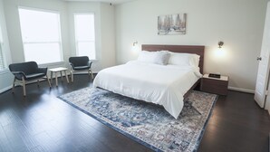 Une chambre à coucher avec un grand lit, deux tables de chevet, une commode, un ventilateur de plafond et une fenêtre avec des stores.