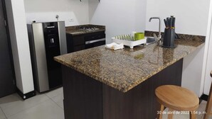 Una cuina moderna amb armaris foscos, un frigorífic d'acer inoxidable, una cuina a gas i un taulell de granat.