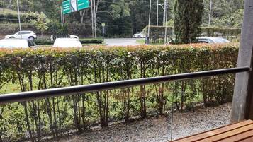 Vista desde un balcón con barandilla de madera, sobre una calle con coches y un cartel direccional verde.