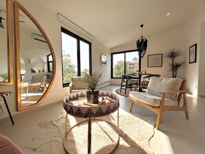 A spacious living room with a large mirror, a round table with a plant, and a comfortable seating area with a sofa and chairs.