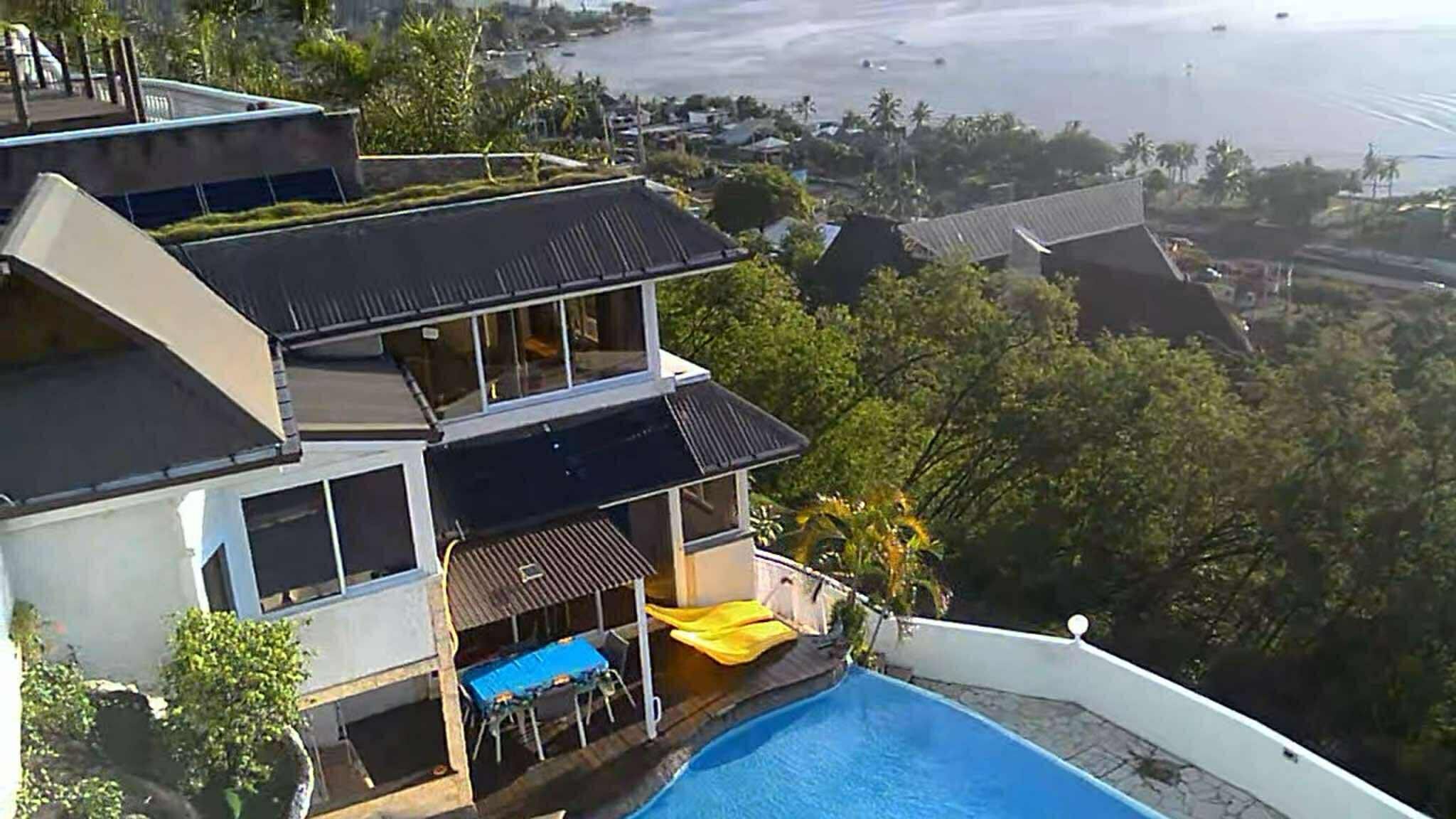 A modern two-story house with a swimming pool, large windows, and a view of the beach.