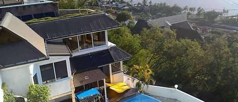 A modern two-story house with a swimming pool, large windows, and a view of the beach.