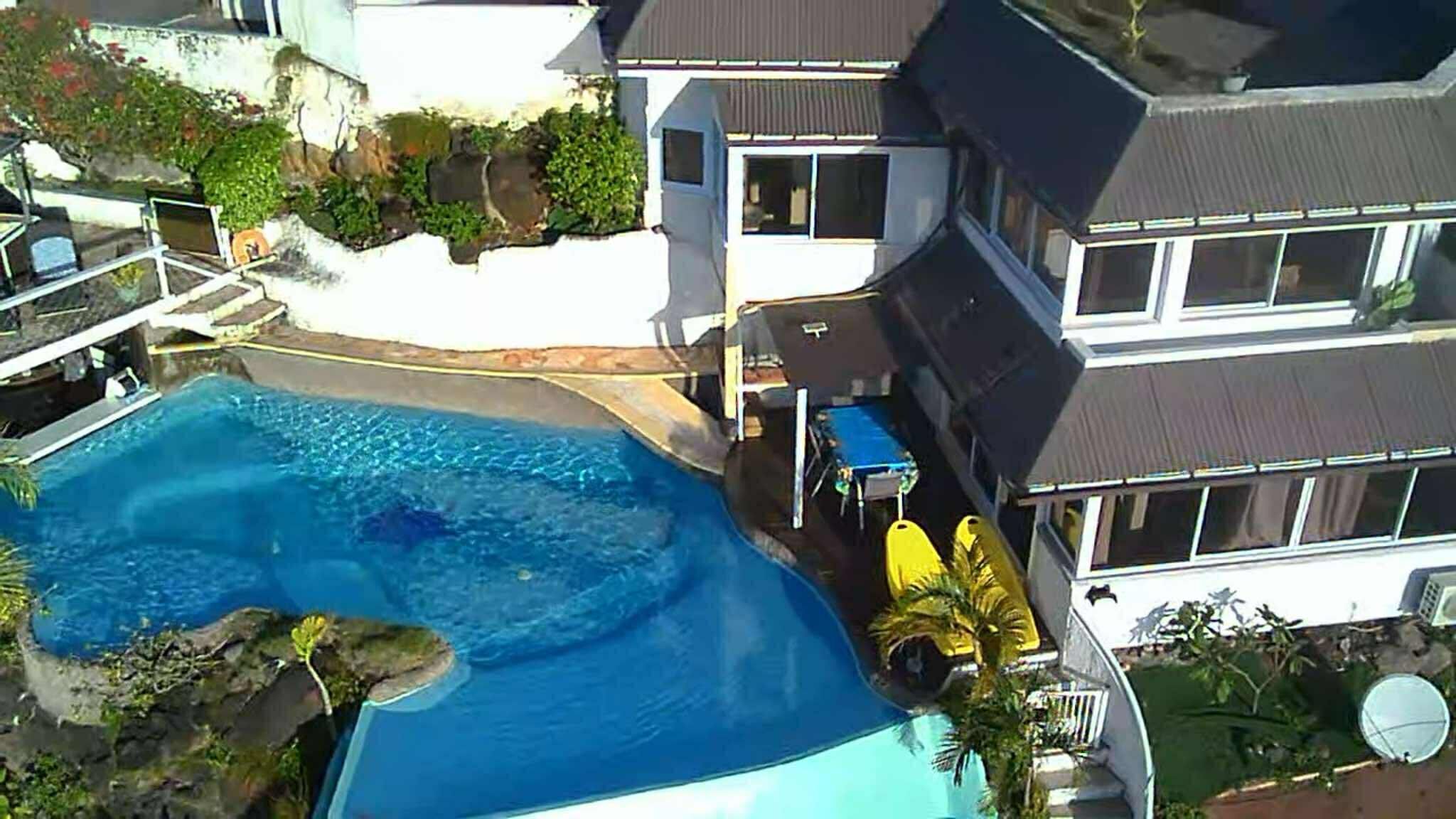 A residential property with a swimming pool, a covered patio, and a large house with multiple windows.