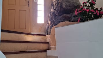 Una escalera con peldaños color beige y barandillas de madera, que conduce a una puerta beige con un ventanal encima.