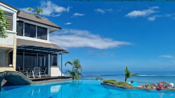 En swimmingpool med havudsigt, en overdækket terrasse og et hus med balkon.