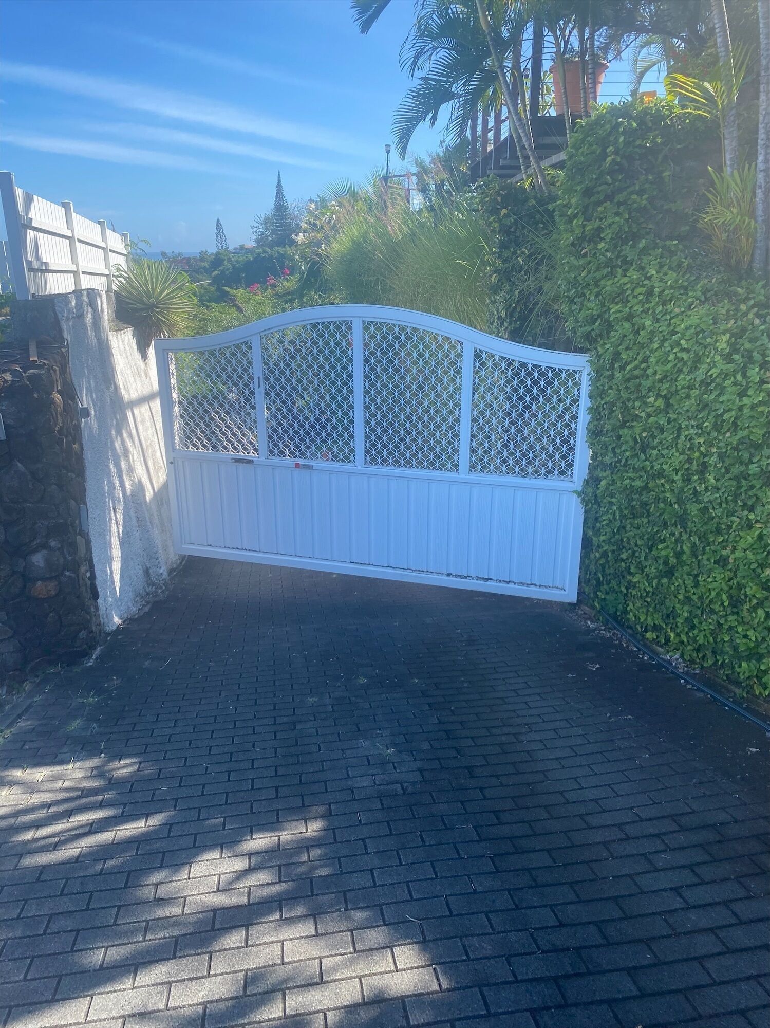 A gated entrance with a white decorative fence, paved pathway, and lush greenery.