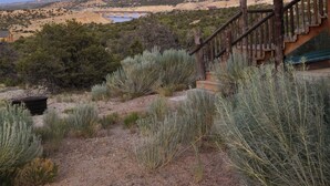 Un escalier rustique mène à un bâtiment en bois, d’où l’on peut admirer un paysage désertique et, au loin, une étendue d’eau.