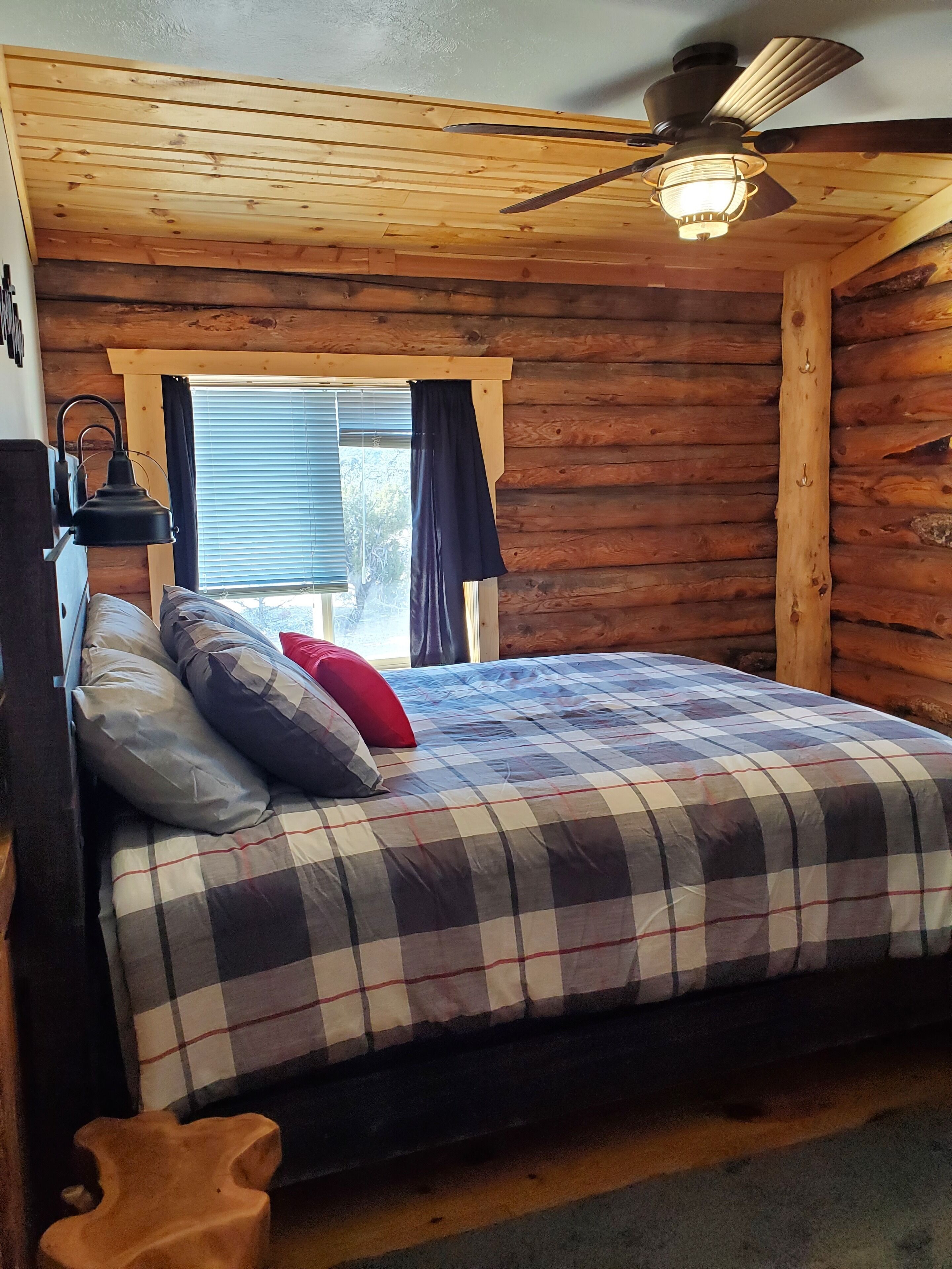 Ein Schlafzimmer einer Holzhütte mit Bett, Deckenventilator und einem Vorhangfenster.