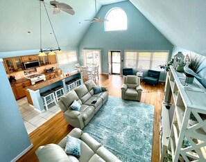 A spacious living area with a large sofa, a coffee table, and a dining table. There is a kitchen in the background with a microwave and a stove. - Newly-Renovated, Open-Concept Private Beach House in Margate - Pet-Friendly! (Margate City)
