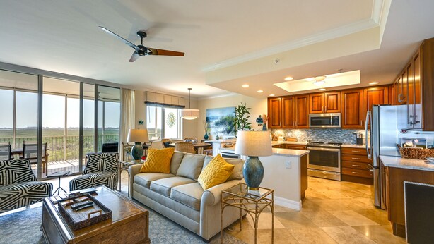 A spacious living room with a large window, a ceiling fan, and a modern kitchen with wooden cabinets and stainless steel appliances. - Estero Resort Condo w/ 2 Pools & Tennis Center! (Estero)