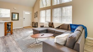 Ein geräumiges Wohnzimmer mit einer Eckcouch, einem Couchtisch und einem großen Fenster mit Jalousien.