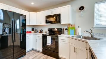 A modern kitchen with white cabinets, a black refrigerator, a microwave, and a stove.