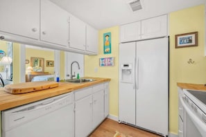 Une cuisine compacte avec des meubles blancs, un plan de travail en bois, un lave-vaisselle encastré et un réfrigérateur.