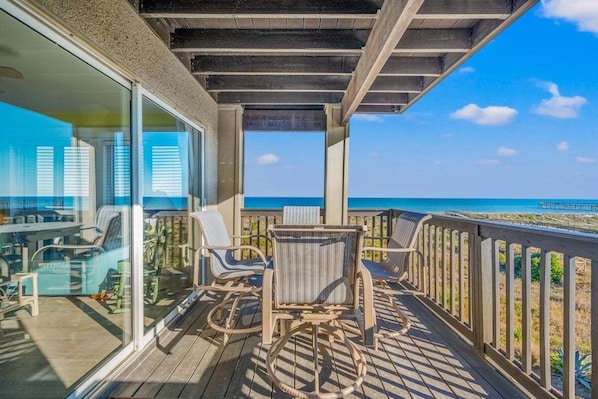 A balcony with wicker chairs and a table, overlooking a beach.