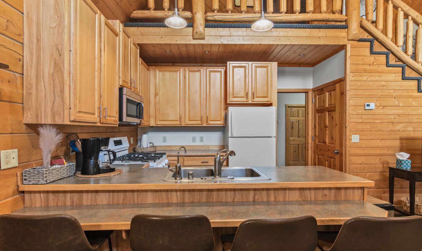 A wooden cabin-style kitchen with a central island, wooden cabinets, a microwave, a stove, and a refrigerator.