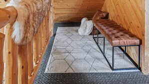 Een houten blokhut van binnen, met een bankje, een spiegel en een bont bekleed object.