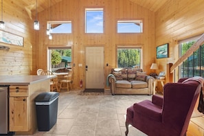 A wooden cabin interior with a dining area, a sofa, and a staircase.