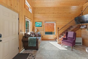 A wooden interior with a sofa, armchair, and a staircase. - Kenai Cozy Cabin - 2 (Kenai)
