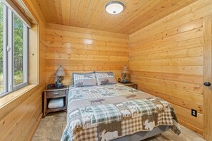 A wooden cabin bedroom with a bed, two bedside tables, a window, and a ceiling light.