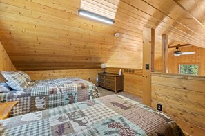 A cozy cabin room with two beds, a dresser, and a ceiling fan. - Kenai Cozy Cabin - 2 (Kenai)