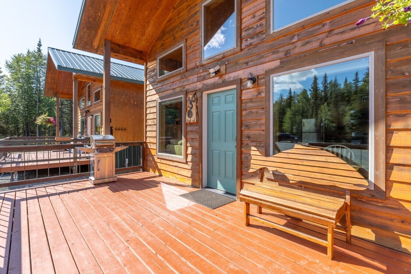 A wooden cabin with a deck, a barbecue, and a door with a number.