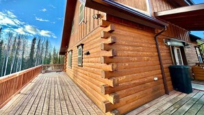 A wooden cabin with a deck, a chimney, and a window overlooking a forest.