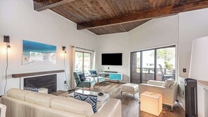 A modern living room with a fireplace, a flat-screen TV, and a large window. - Canal Front Golf Retreat w/Dock (Ocean Pines)