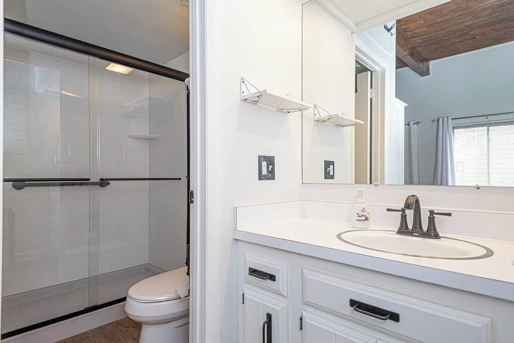 A bathroom with a glass shower enclosure, a white sink with a mirror above it, and a white toilet.