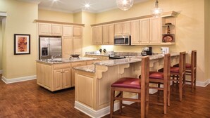 A kitchen with wooden cabinets, a stainless steel refrigerator, a microwave, and a coffee maker. There are wooden bar stools with red cushions. - 3BD Deluxe/Branson - w/Pools, BBQ, Game Room, Gym! (Branson)