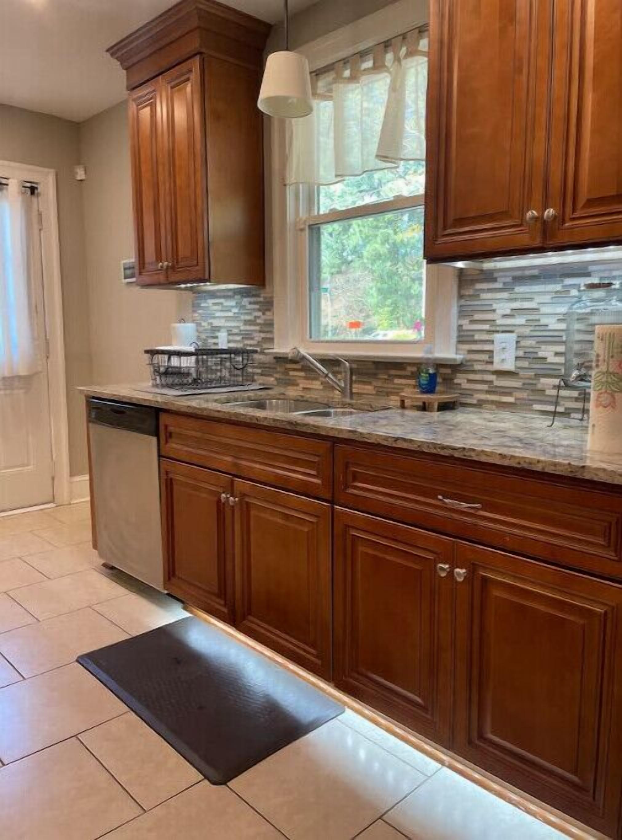 A kitchen with wooden cabinets, a stone backsplash, a window with curtains, and a pendant light.