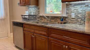 A kitchen with wooden cabinets, a stone backsplash, a window with curtains, and a pendant light.