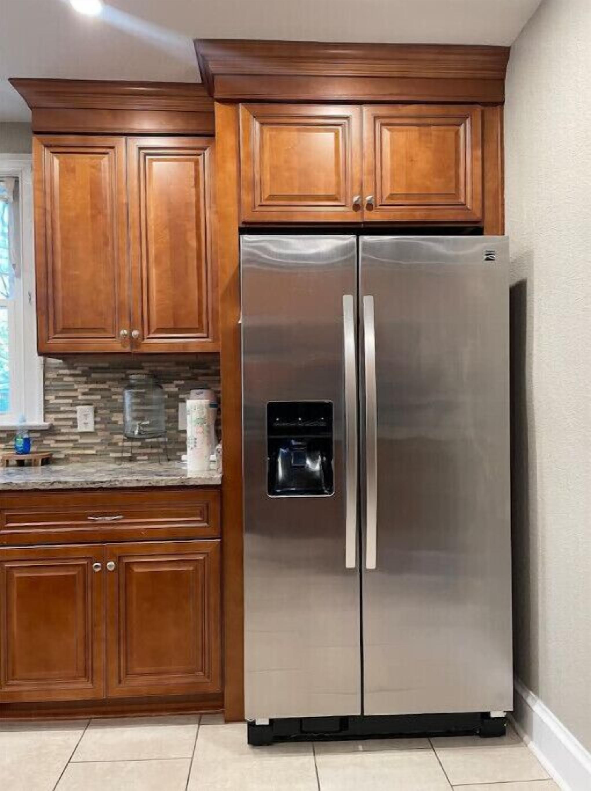 A stainless steel refrigerator with a water dispenser, wooden cabinets, and a tiled backsplash in a kitchen.
