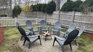 A circular outdoor seating area with six Adirondack chairs and a central fire pit. - Private Falmouth home perfect for family fun - hot tub, fire pit, and game room! (Falmouth)