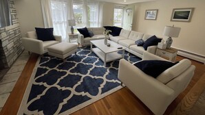 A modern living room with a stone accent wall, a patterned rug, and a neutral color scheme. - Private Falmouth home perfect for family fun - hot tub, fire pit, and game room! (Falmouth)
