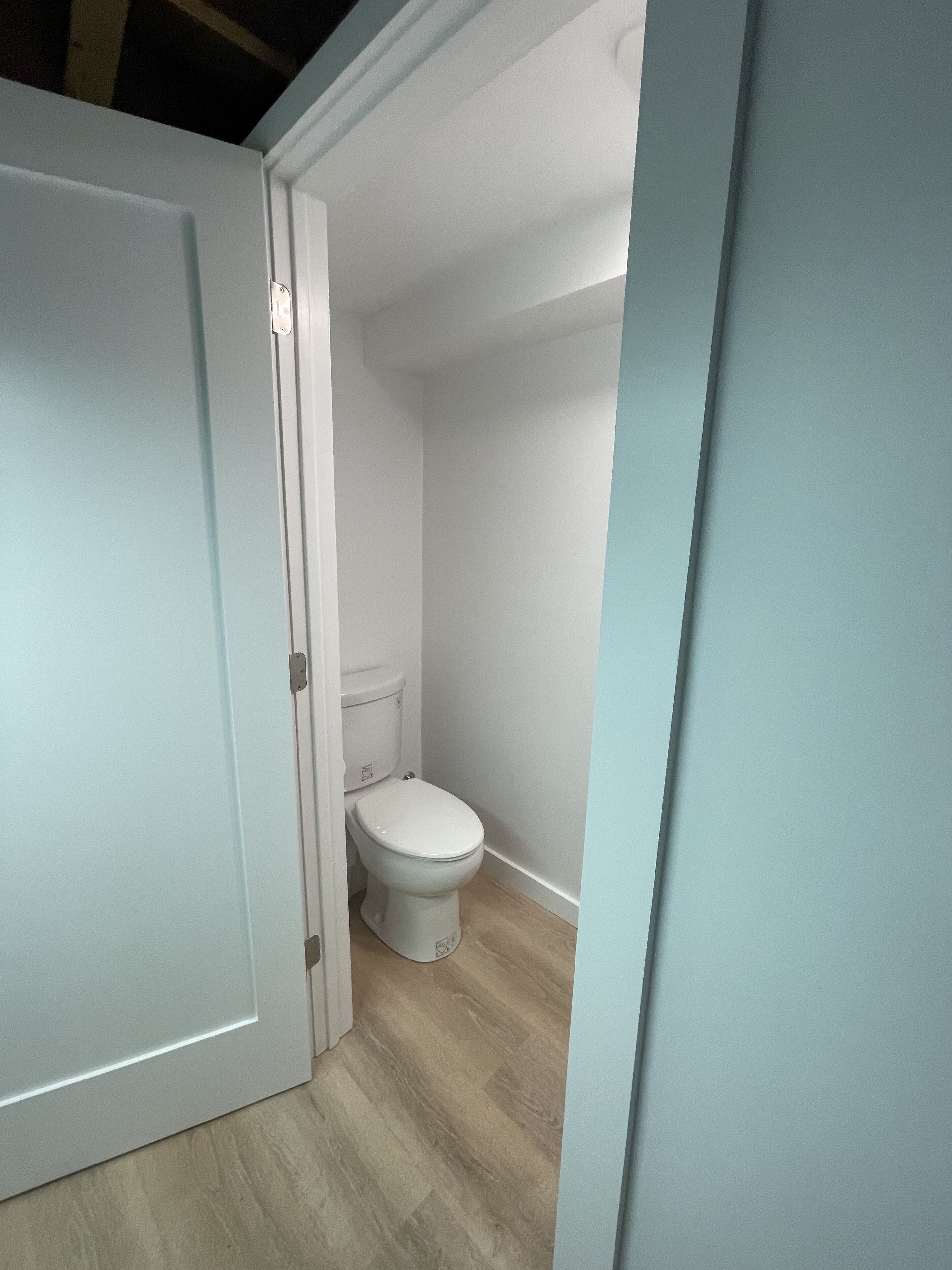 A small, narrow bathroom with a white toilet and a wooden floor.