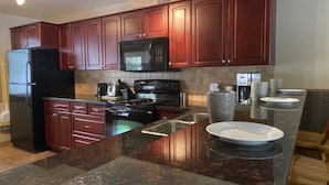 A modern kitchen with dark wooden cabinets, a black refrigerator, a microwave, a stove, and a sink.