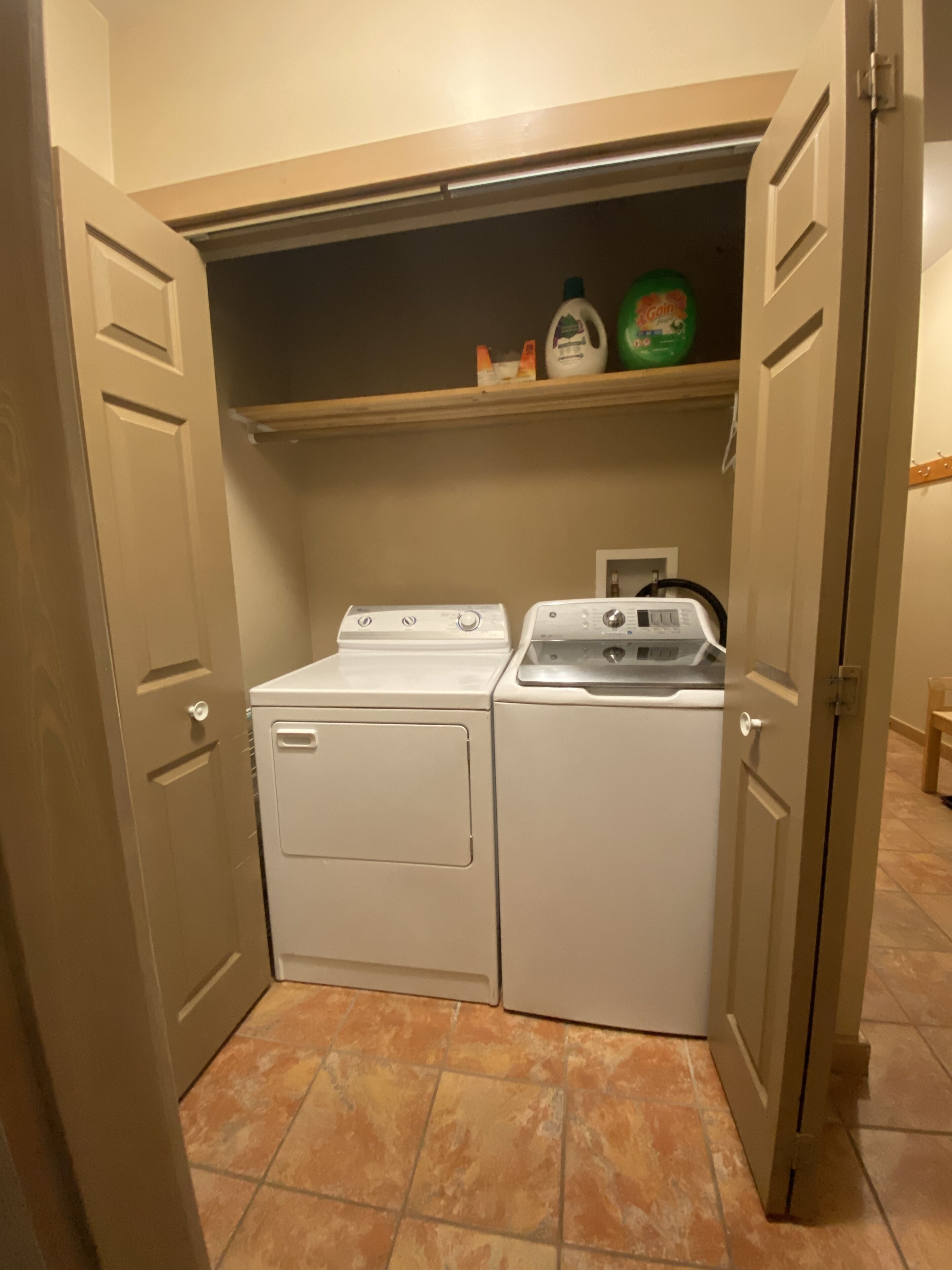 Une buanderie équipée d’un lave-linge et d’un sèche-linge, avec une étagère au-dessus pour ranger les produits de nettoyage, et un sol carrelé.