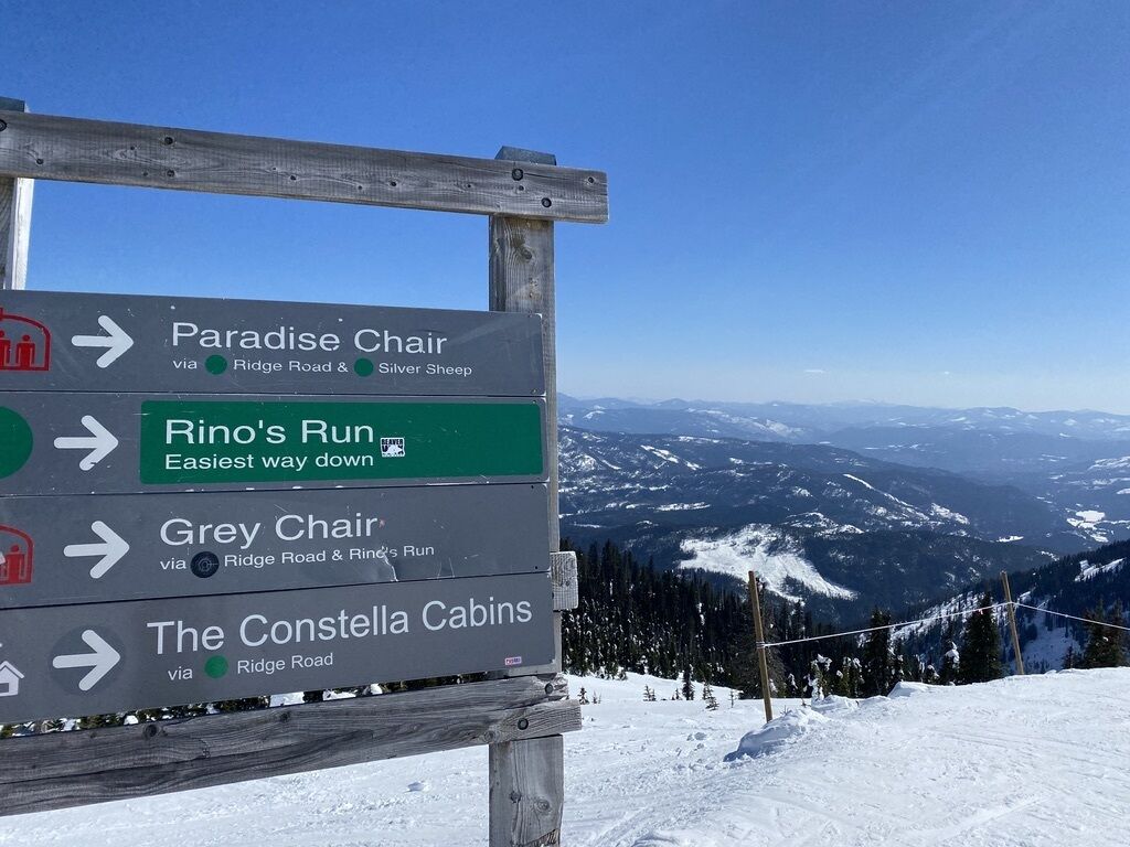 Un panneau indicateur indiquant plusieurs destinations, notamment le télésiège de Paradise, la piste de Rino, le télésiège de Grey et les chalets de Constellia, toutes accessibles par la route de Ridge.