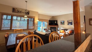 A spacious living room with a fireplace, a dining area with wooden chairs, and a large TV mounted on the wall.