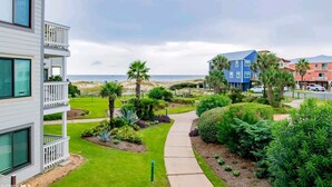 A multi-story building with balconies, a landscaped garden with palm trees, and a view of the beach. - Sugar Sands-Luxury 1st Floor 2BR 2BA Private Beach (Gulf Shores)
