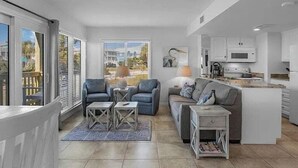 A modern living room with a grey sofa, two armchairs, and a coffee table. There is a kitchen area with white cabinets and a microwave. - Sugar Sands-Luxury 1st Floor 2BR 2BA Private Beach (Gulf Shores)