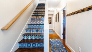 A staircase with patterned tiles and a wooden handrail, leading to a hallway with a patterned rug and framed pictures on the wall. - Gorgeous Moab Retreat with Red Rock and La Sal Mountain Views - South Valley (Moab)