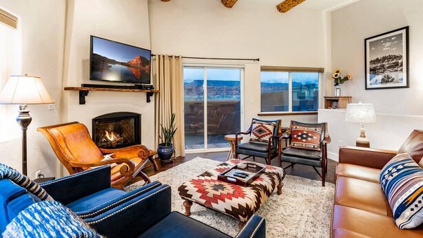 A spacious living room with a fireplace, comfortable seating, a large TV, and a view of the outdoors. - Gorgeous Moab Retreat with Red Rock and La Sal Mountain Views - South Valley (Moab)